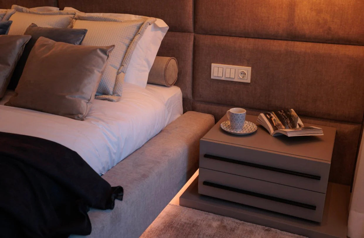Bedroom scene with a bed, nightstand, and wall socket.